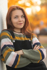 Portrait of a young beautiful red-haired girl in an autumn city park.