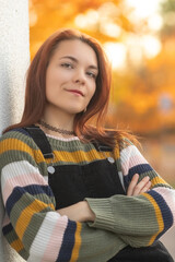 Portrait of a young beautiful red-haired girl in an autumn city park.