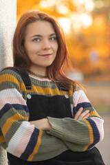 Portrait of a young beautiful red-haired girl in an autumn city park.