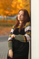 Portrait of a young beautiful red-haired girl in an autumn city park.