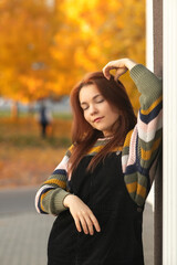 Portrait of a young beautiful red-haired girl in an autumn city park.