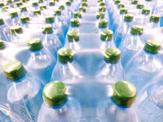 Multiple plastic water bottles tightly packed in shrink wrap, seen from above. Green caps, blue-toned bottles, clean, fresh visual, hydration, mass production, bottled water industry, packaging