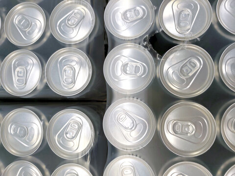 Top view of aluminum drink cans tightly packed in shrink wrap. repetitive pattern of can tops, beverage industry, mass production, and recycling