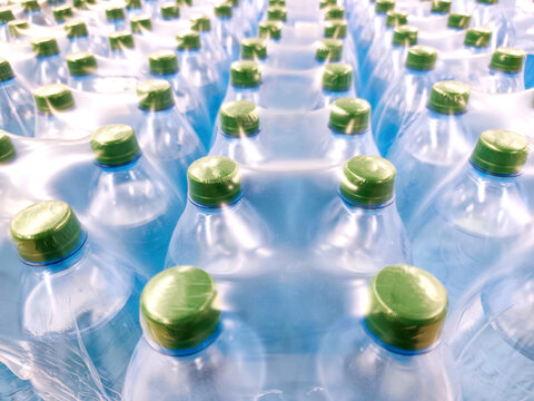 Multiple plastic water bottles tightly packed in shrink wrap, seen from above. Green caps, blue-toned bottles, clean, fresh visual, hydration, mass production, bottled water industry, packaging