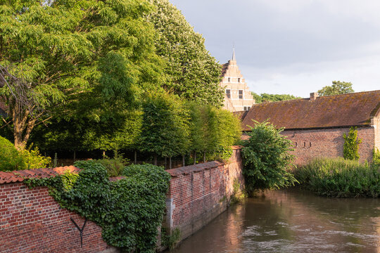 Scenic view of the Dijle river canal flowing along the historic brick walls of the Groot Begijnhof in Leuven, Belgium.