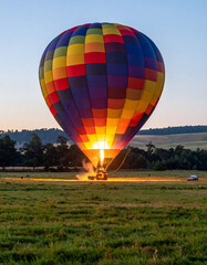 Spectacular, colorful hot air balloon being inflated with fire on a grassy field at dusk. Represents adventure, travel, dreams, and special events.