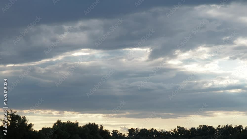 Aufkleber Witness the captivating journey of light slicing through layered clouds during twilight, showcasing natures artistry in a serene landscape. A transformative display unfolds overhead