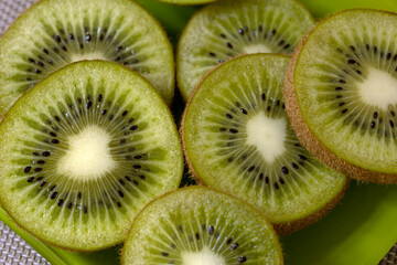 Sliced kiwi fruit arranged on a green plate. The vibrant green flesh and small black seeds are clearly visible, showcasing the fruit's unique texture and color.