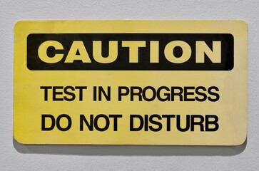 Caution test in progress do not disturb sign notice on wall industrial occupation.