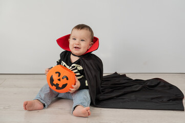 Cute caucasian boy in dracula halloween costume holding candy basket on white background. 