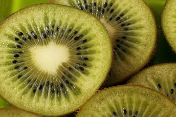 Sliced kiwi fruit showing vibrant green flesh and small black seeds. The texture is smooth with a...