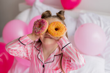 little girl celebrates her birthday morning in pink pajamas with donuts