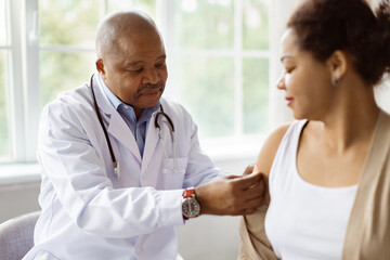 Antiviral Vaccination. Black doctor sticking plaster bandage on patients shoulder after injection...