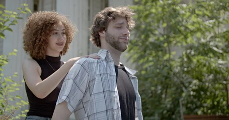 A young woman gives a relaxing shoulder massage to a young man outdoors on a sunny day. He closes his eyes and smiles in enjoyment and relief. - Powered by Adobe