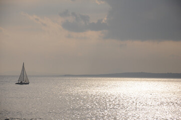 Sailboat navigates shimmering waters beneath tranquil, overcast sky
