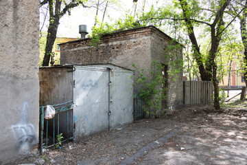Old brick utility building with a metal shed and overgrown trees in a quiet residential yard