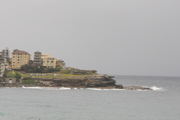 Overcast rocky coastline with buildings overlooking calm sea