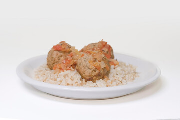 Side view of a plate with rice and three meatballs on a white background.