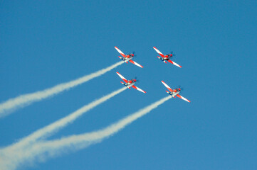 Four aerobatic planes perform maneuvers with smoke trails in blue sky