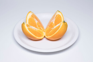 Close-up of an orange cut into four pieces on a white plate and against a white background..