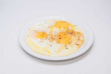 Close-up of a plate with three fried eggs with paprika and black pepper on top., on a white background.