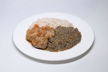 Close-up of a plate with three meatballs with raice and lentils, on a white background.