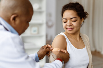 Doctor applying adhesive bandage to patients upper arm after vaccination, smiling african american...
