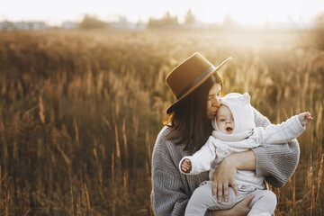 Happy mother hugging and kissing cute baby son in autumn field in soft evening light. Parenthood....