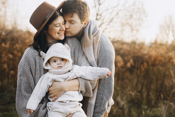 Happy family hugging and kissing with cute baby son in autumn field in soft evening light....