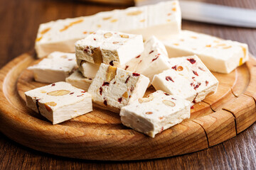White nougat bars with almonds and dried fruit on cutting board on wooden table.
