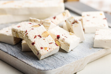 White nougat bars with almonds and dried fruit on cutting board on white table.
