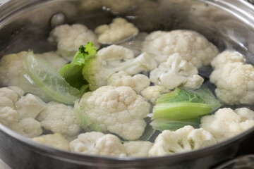 Fresh cauliflower is boiled in a saucepan with water. The vegetable is divided into florets and boiled in a saucepan.