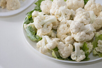 Fresh and raw cauliflower on the white plate.  The cauliflower  -  vegetable is cut into pieces on white background. The vegetable is divided into inflorescences on the plate