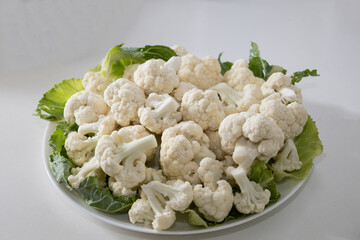Fresh and raw cauliflower on the white plate.  The cauliflower  -  vegetable is cut into pieces on white background. The vegetable is divided into inflorescences on the plate