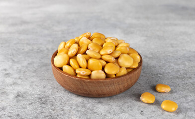 Pickled yellow lupine beans in a wooden bowl on a grey background. High protein plant food.