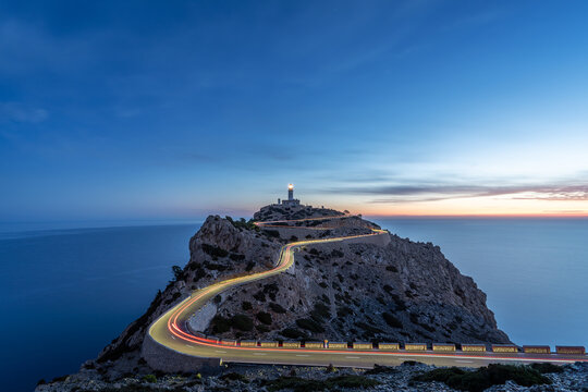 Blue hour image of light trails on winding hairpin road, leading to the Far the Formentor lighthouse, positioned on dramatic cliff landscape next to the ocean on Mallorca, Spain