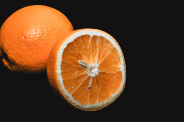 Two oranges, one whole and one cut in half, on a black background