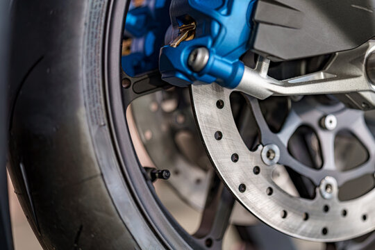 Detail of motorcycle brake system showcasing caliper, rotor, and tire in a workshop setting - Powered by Adobe