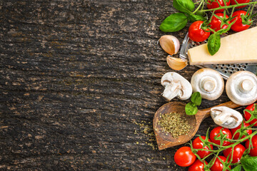 Fresh ingredients for cooking Italian food including cherry tomatoes, mushrooms, parmesan, garlic, oregano and basil on dark rustic wooden background with copy space