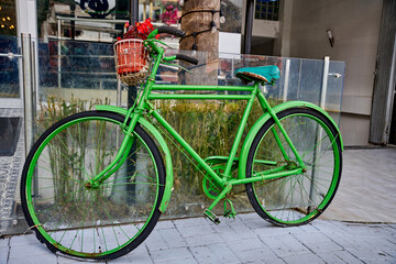 Bright-green vintage road bicycle with flower basket repurposed as street decor outside a local cafe, enhancing urban charm and inviting atmosphere