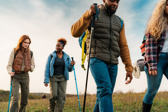 Diverse group hiking in a grassy field, carrying trekking poles and wearing outdoor clothing.