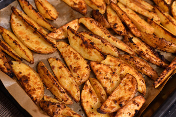 baked Country-style potatoes - wedges with skins in spices on baking sheet.