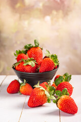 Pot with strawberries, a beautiful little black pot full of delicious strawberries on rustic wood, selective focus.