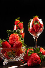 Bowls with strawberries, beautiful crystal bowls full of delicious strawberries on dark surface, black background, selective focus.