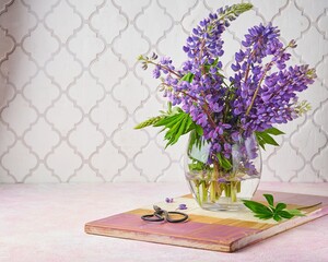 Bouquet of blue lupine in a transparent glass vase on a pink concrete background.