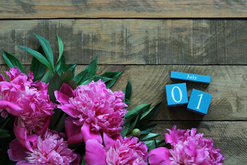Pink peonies and a calendar showing july 1st on rustic wooden background