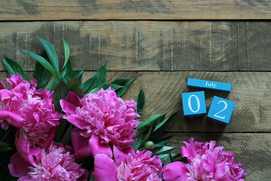 Pink peonies and wooden calendar showing july 2nd on rustic table