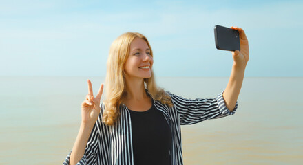 Happy cheerful young woman smiling taking selfie with smartphone on the beach, joyful girl on sea