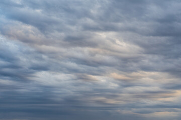 An abstract natural background of textured clouds in the evening light. A beautiful, wavy pattern of gray and blue clouds in the sky.