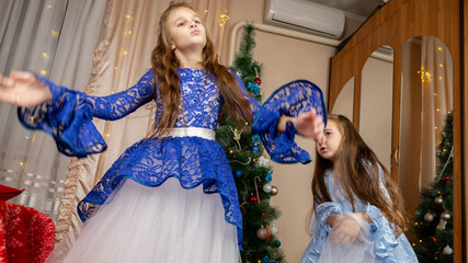 Little girls in festive dress dancing near christmas tree at home